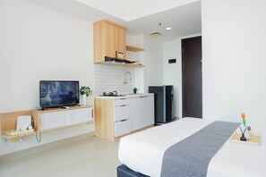 Ein modernes Hotelzimmer mit Bett, Fernseher, Küchenzeile und einer dunklen Tür.