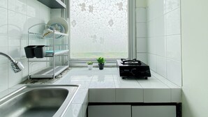 Una cocina moderna con un lavamanos de acero inoxidable, una ventana con estampado floral y una estantería con vajilla.