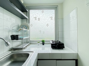 Eine moderne Küche mit einer Edelstahl-Spüle, einem Fenster mit floralem Muster und einem Regal mit Geschirr.
