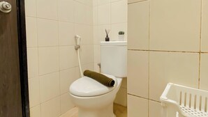 Un baño con inodoro, ducha y una cesta de plástico blanca para la ropa.
