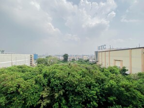 A rooftop view with dense greenery in the foreground, a clear sky, and distant buildings. - Good Deal Studio Apartment Mont Blanc Bekasi (Bekasi)