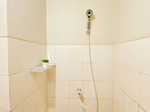 Eine Dusche mit Duschbrause, Wandarmatur und kleinem Ablagefach mit Topfpflanze.
