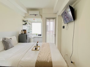 Ein Hotelzimmer mit Bett, Wandfernseher, Küchenzeile und einem fenster mit Vorhängen.