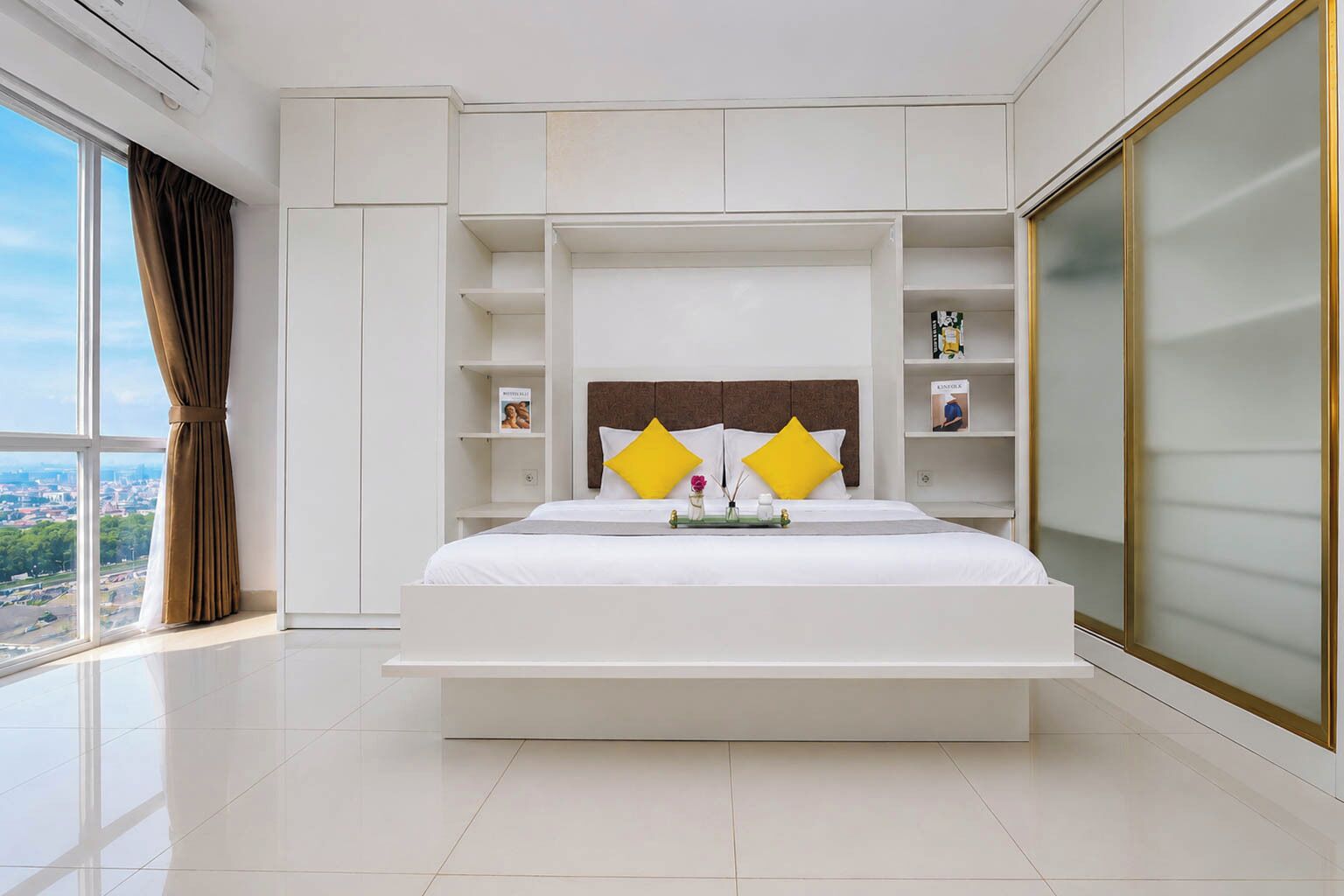 A modern hotel room with a large bed, built-in shelving, and a view of the city.