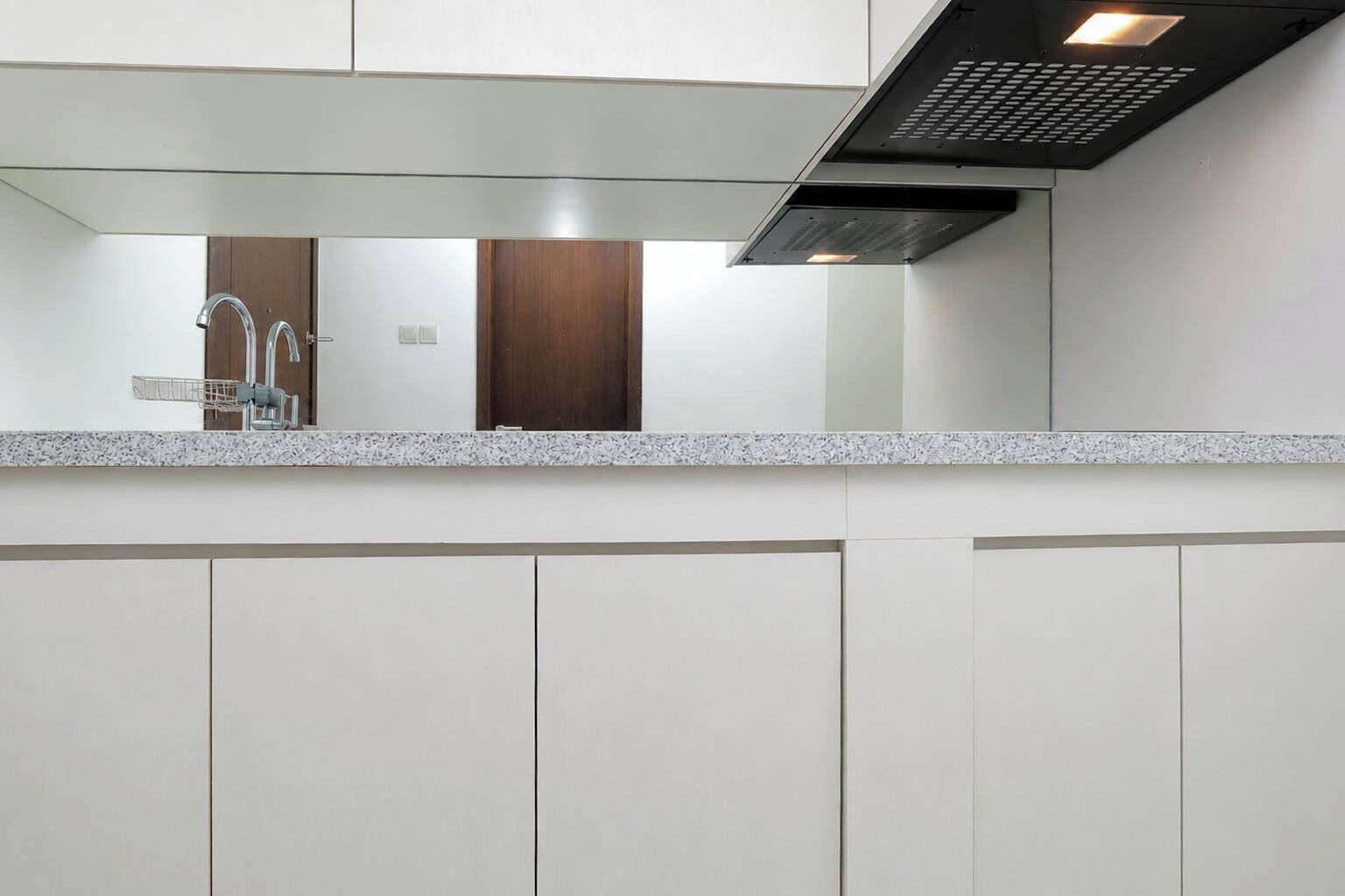 A modern kitchen with a granite countertop, stainless steel faucet, and a black range hood.