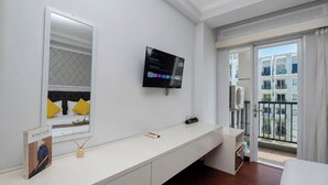 Ett hotellrum med en säng, en tv som är monterad på väggen, ett stort fönster med utsikt över byggnader och ett vitt konsolbord.