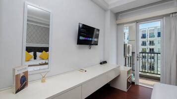 A hotel room with a bed, a TV mounted on the wall, a large window with a view of buildings, and a white console table.