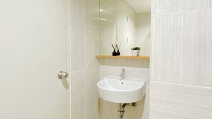 Casa de banho com lavatório branco, espelho e prateleira com planta e recipiente.