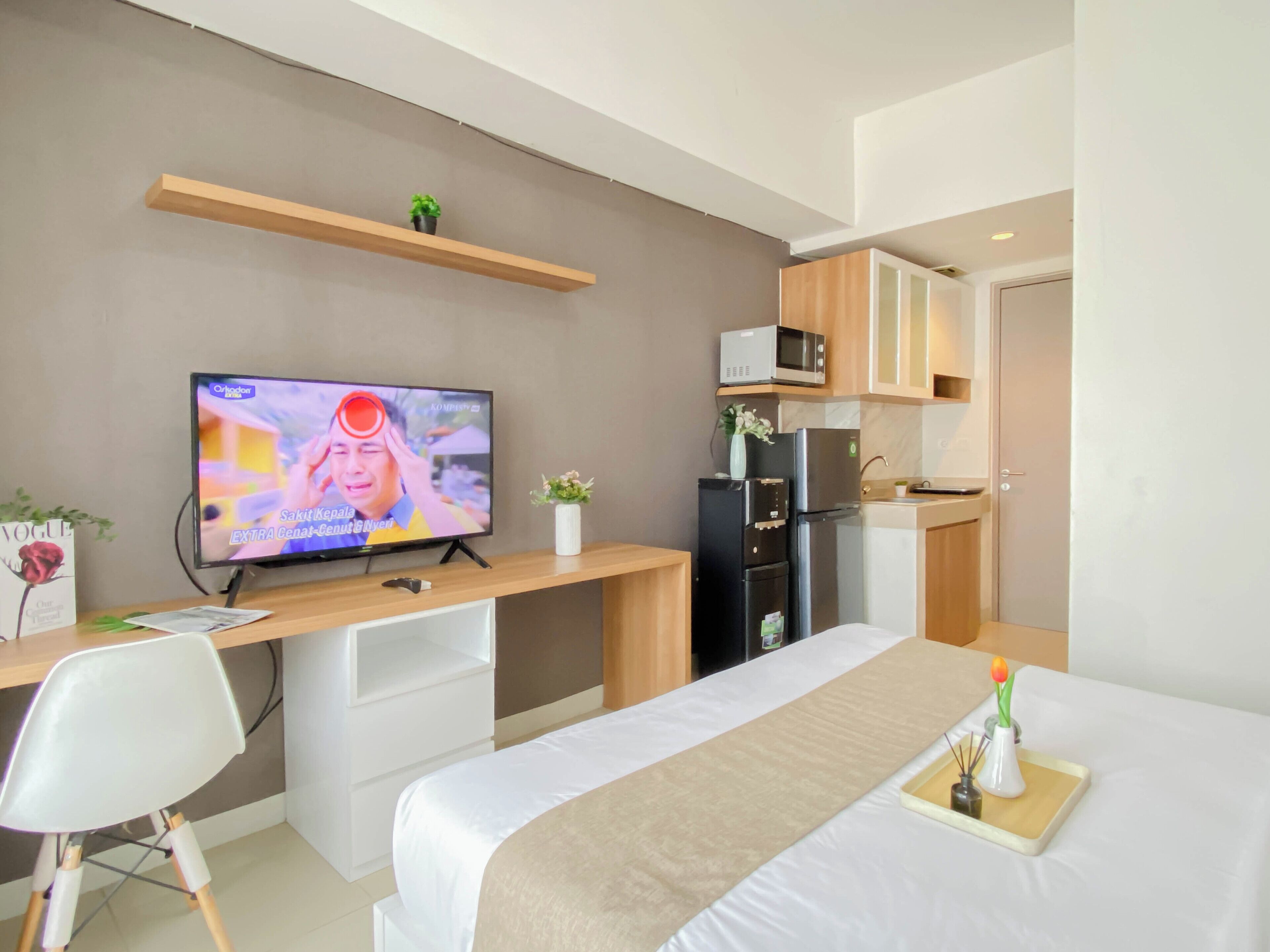 A modern hotel room with a bed, a desk with a television, a microwave, and a refrigerator.