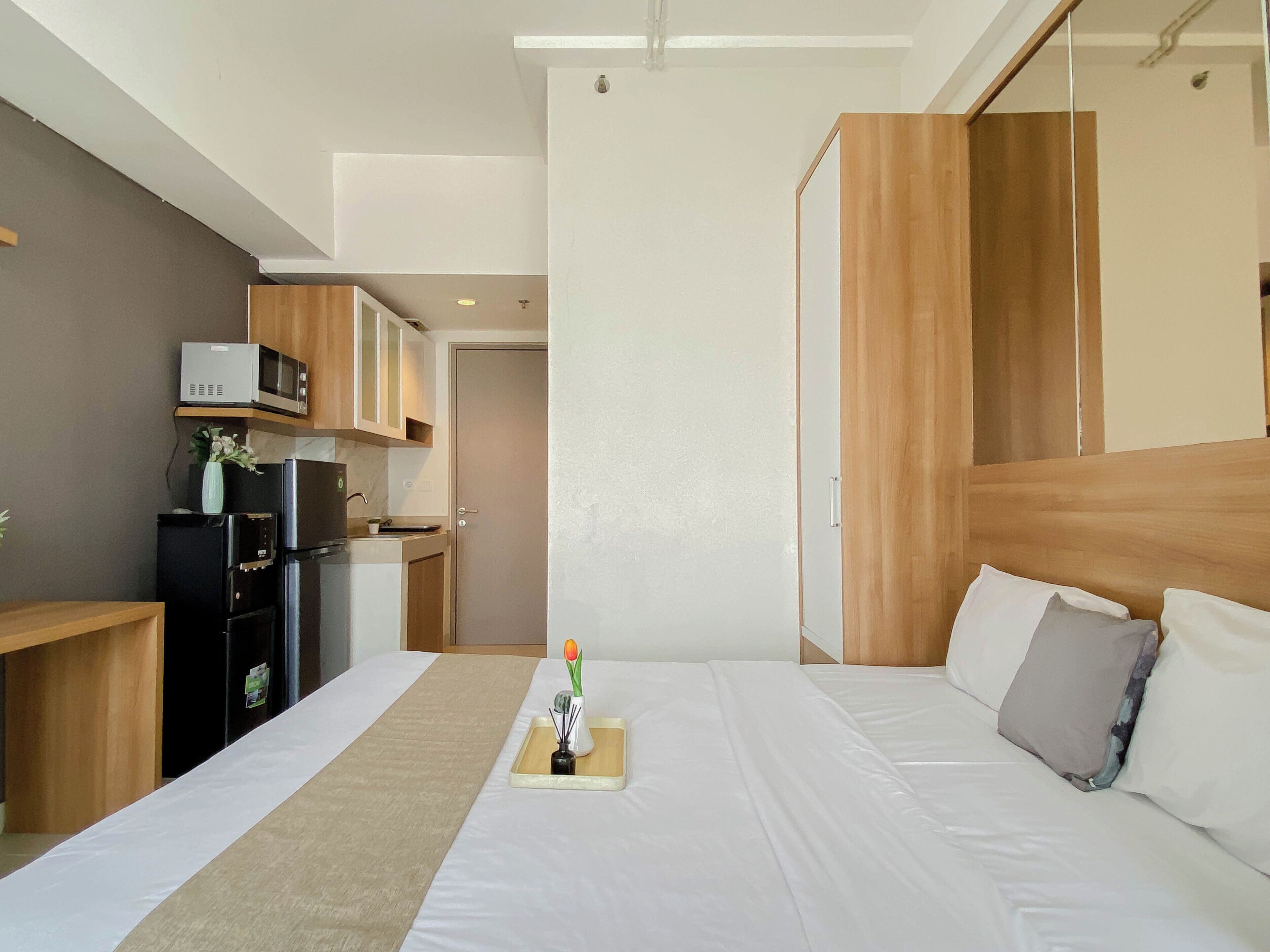 A hotel room with a bed, bedside table, and a kitchenette area with a microwave, refrigerator, and oven.