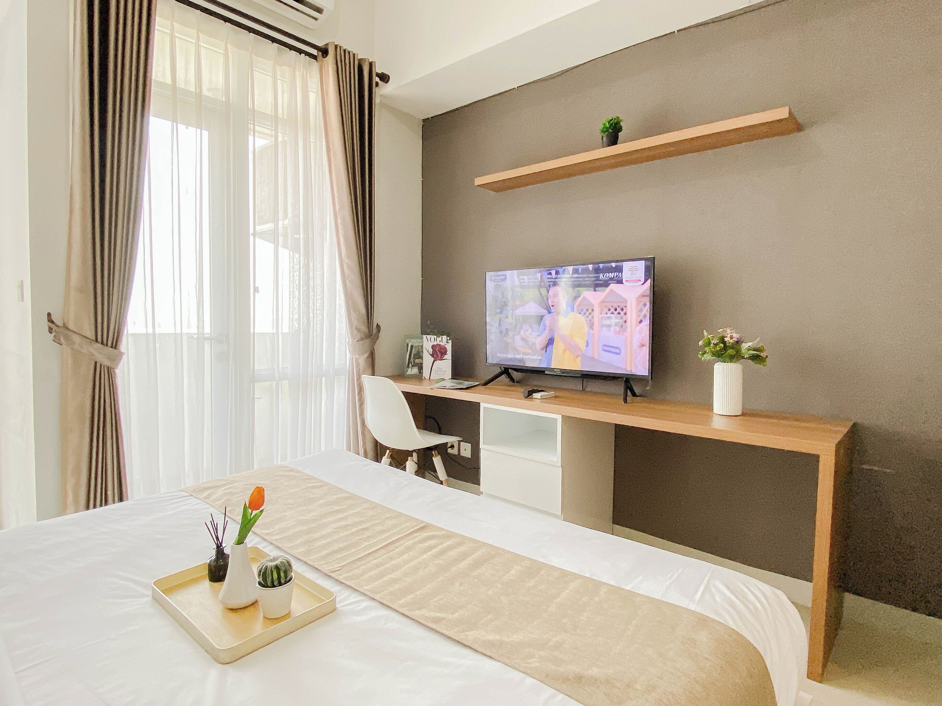 Une chambre d’hôtel avec un lit, un bureau avec une télévision, une chaise et un plateau sur lequel se trouvent une plante et une bougie.