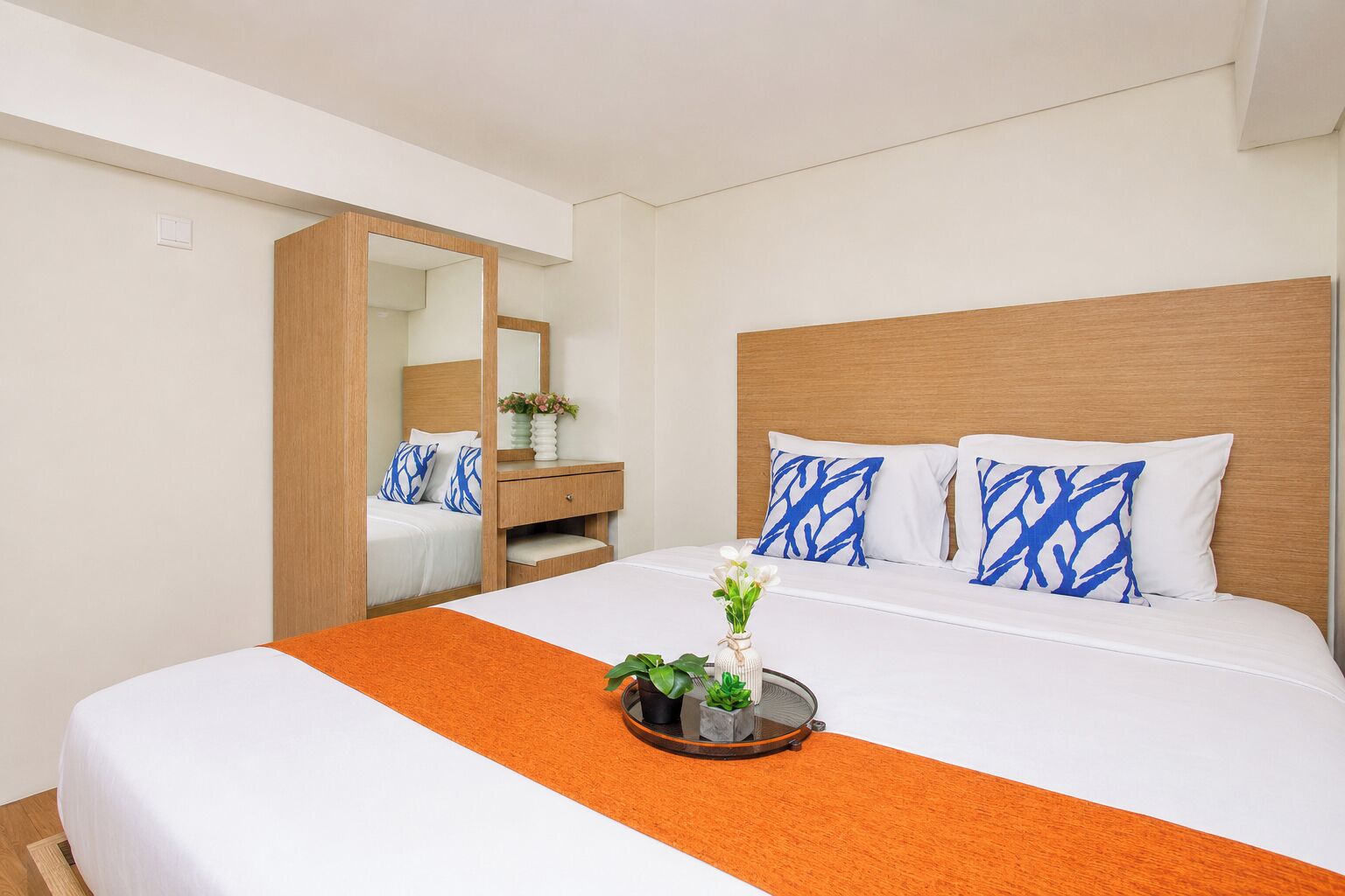 A hotel room with a bed, a nightstand, a dresser, and a mirror.