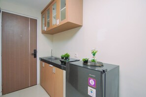 A compact kitchen with a refrigerator, a sink, and wooden cabinets. - Urban Loft Studio At Apartment Apple 1 Condovilla (Jakarta)