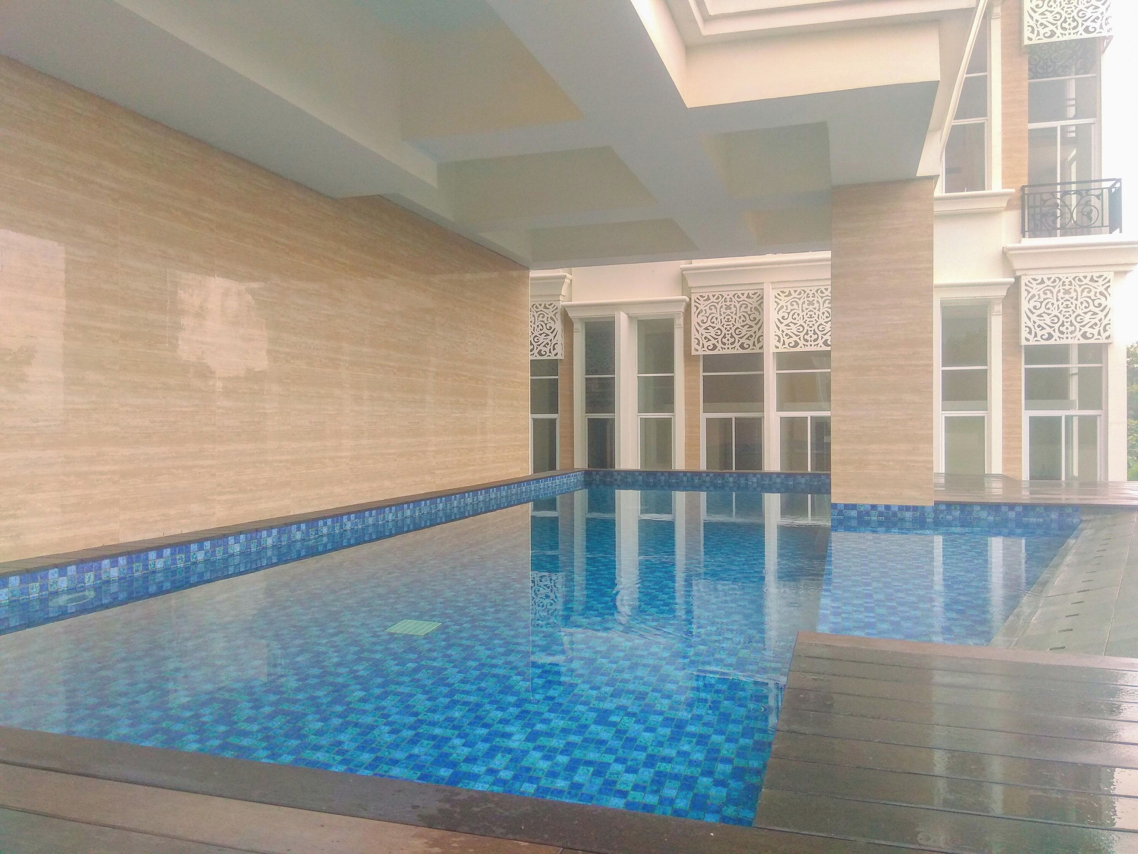 An indoor swimming pool with clear blue water, tiled walls, and a wooden deck.