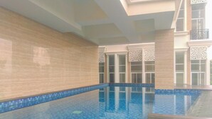 Piscina interna com água azul cristalina, paredes azulejadas e deck de madeira.