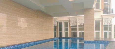 An indoor swimming pool with clear blue water, tiled walls, and a wooden deck.