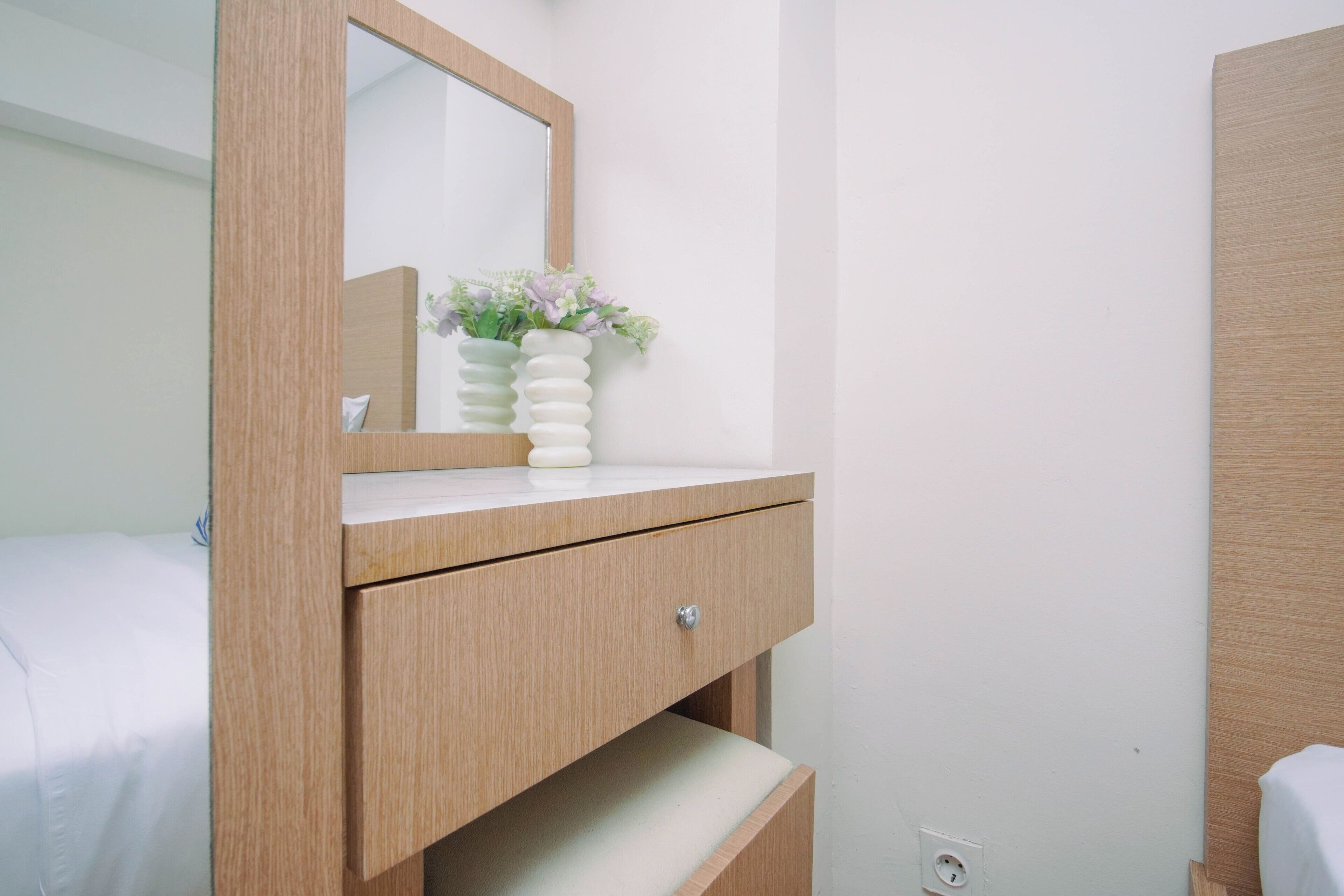 A wooden vanity with a mirror, a white drawer, and a vase with flowers.