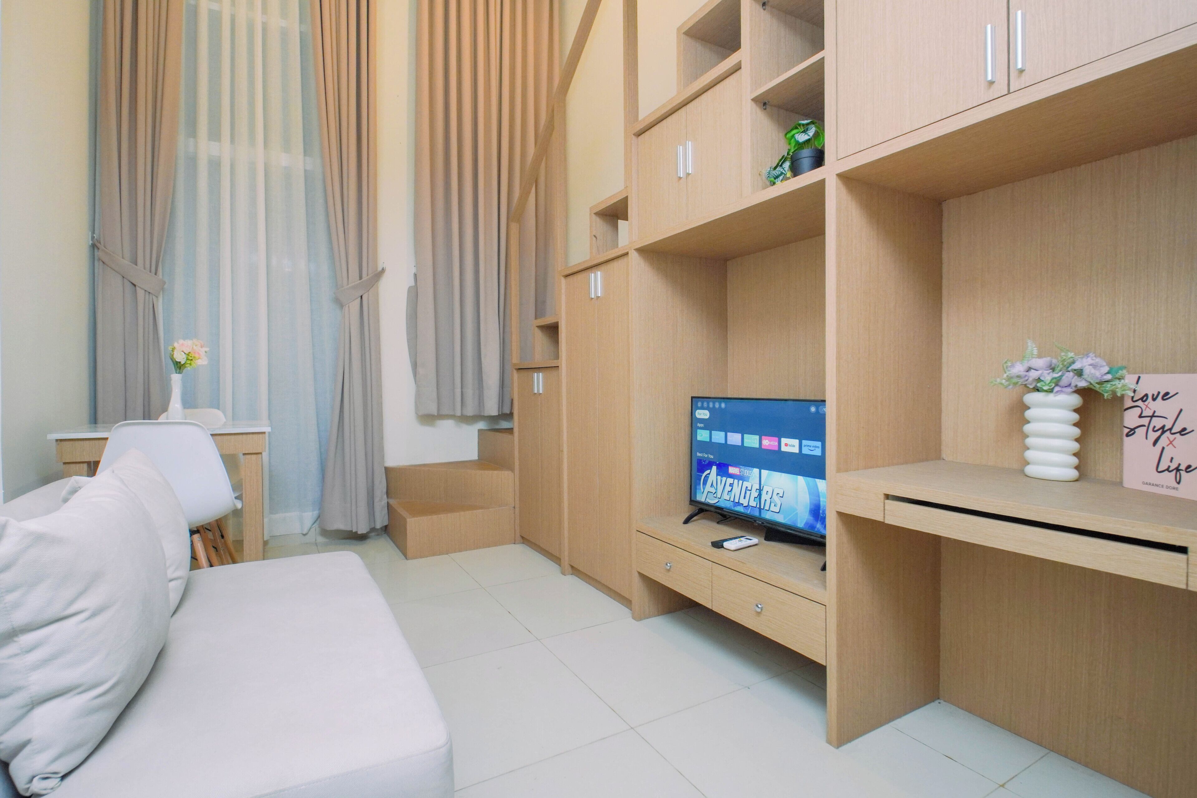 A modern living room with a flat-screen TV, a sofa, a desk, and a bookshelf.