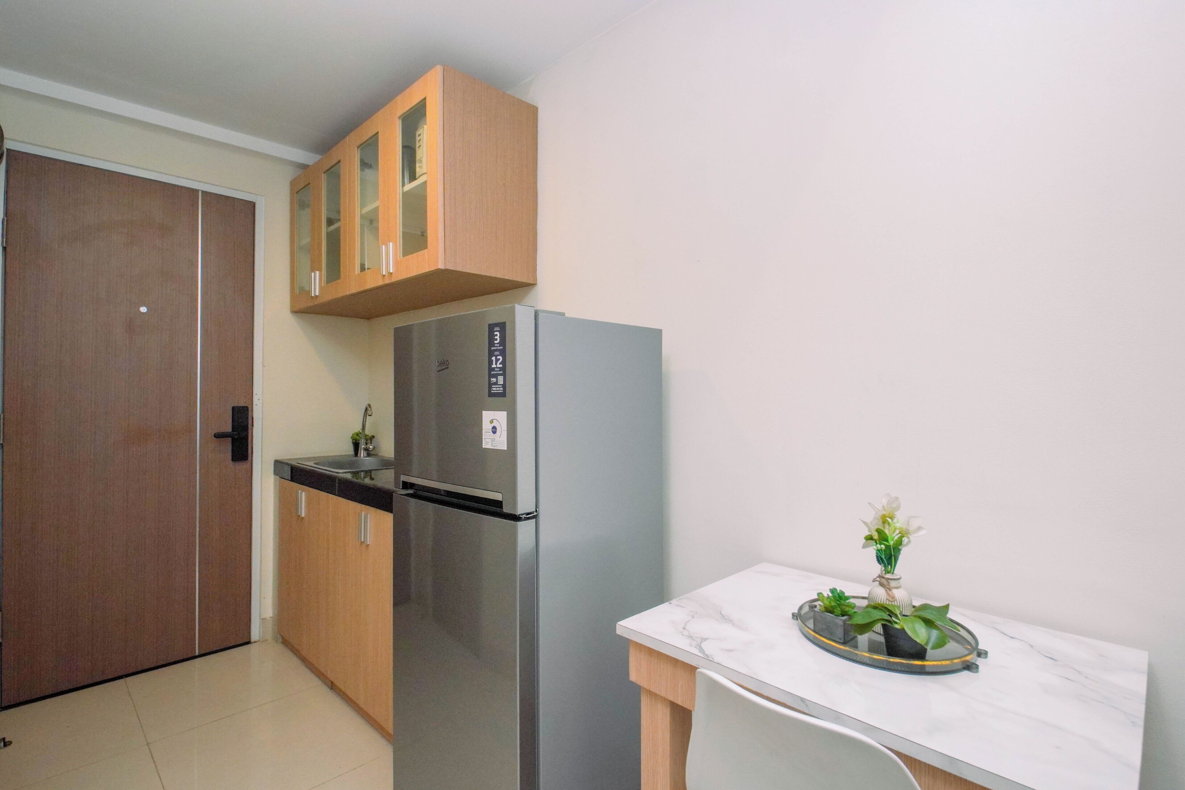 A compact kitchen with a built-in refrigerator, wooden cabinets, and a small table with a vase of flowers.