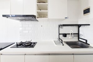 A kitchen with white tiled backsplash, a gas stove, a black range hood, a stainless steel sink, and a black faucet. - Peaceful And Restful Studio Room At Apartment Urbantown Serpong (Tangerang)
