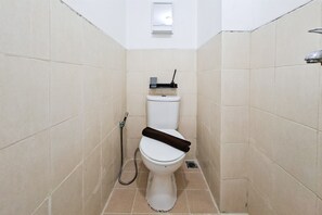 Ein kleines, schmales Badezimmer mit Toilette, Dusche und einer Wandleuchte.