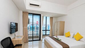 Ett hotellrum med en säng, ett skrivbord, en stol, en TV och en balkong med utsikt över staden.