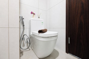 A modern bathroom with a white toilet, a shower, and a dark wooden door. - Nice Look Studio Apartment At Lrt City Bekasi (Bekasi)