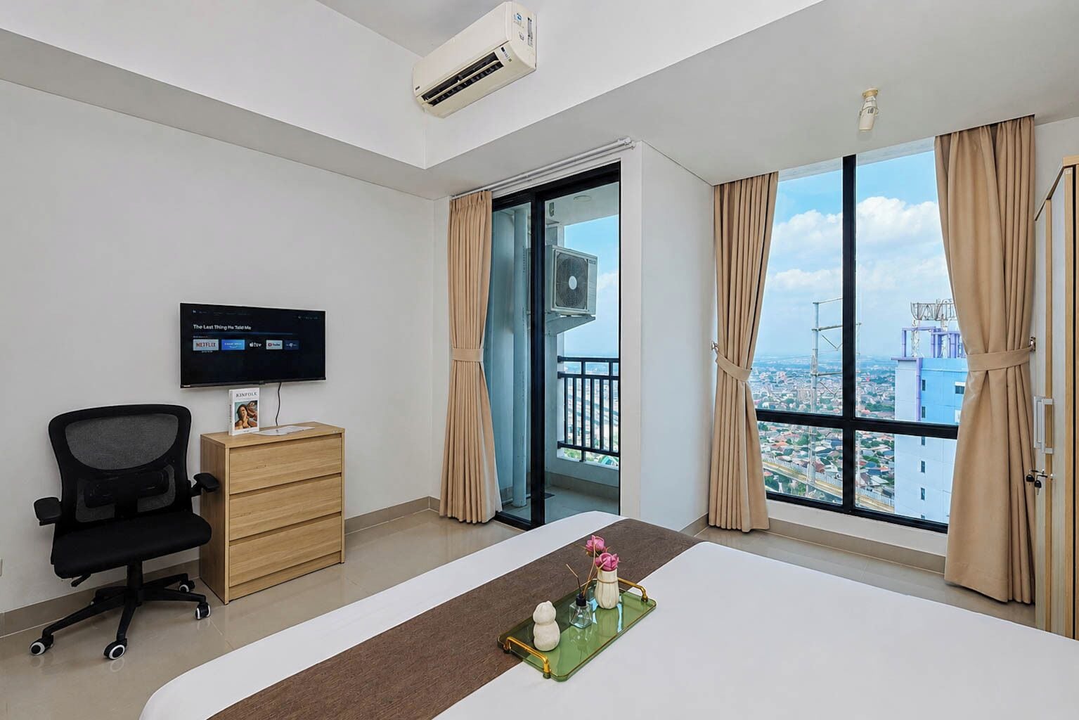 Ein Hotelzimmer mit Bett, Schreibtisch, Stuhl, Fernseher und einem großen Fenster mit Blick auf die Stadt.