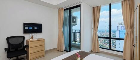Ein Hotelzimmer mit Bett, Schreibtisch, Stuhl, Fernseher und einem großen Fenster mit Blick auf die Stadt.