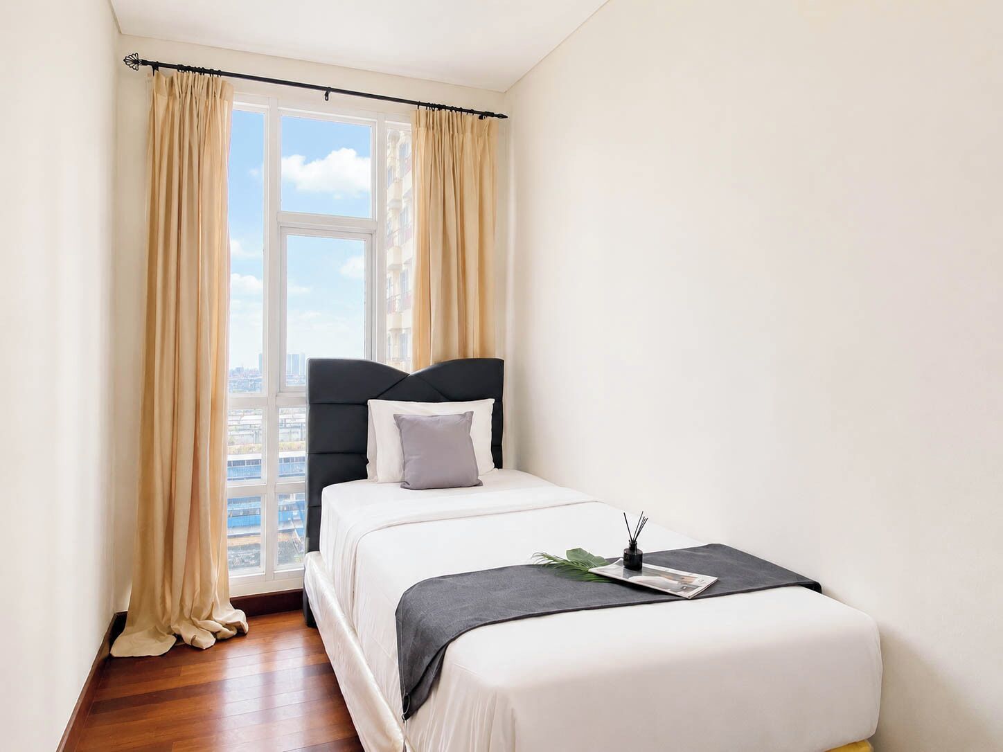 A bedroom with a bed, curtains, a window, and a view of buildings.