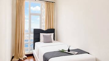 A bedroom with a bed, curtains, a window, and a view of buildings.