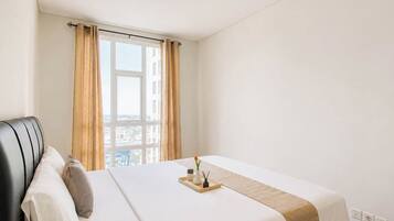 Habitación de hotel con cama, ventana con cortinas, vista a la ciudad y mesita de noche con bandeja.