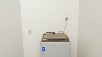 A compact, white water dispenser with a blue label indicating a 7-year warranty, positioned against a plain wall with a single electrical outlet visible.
