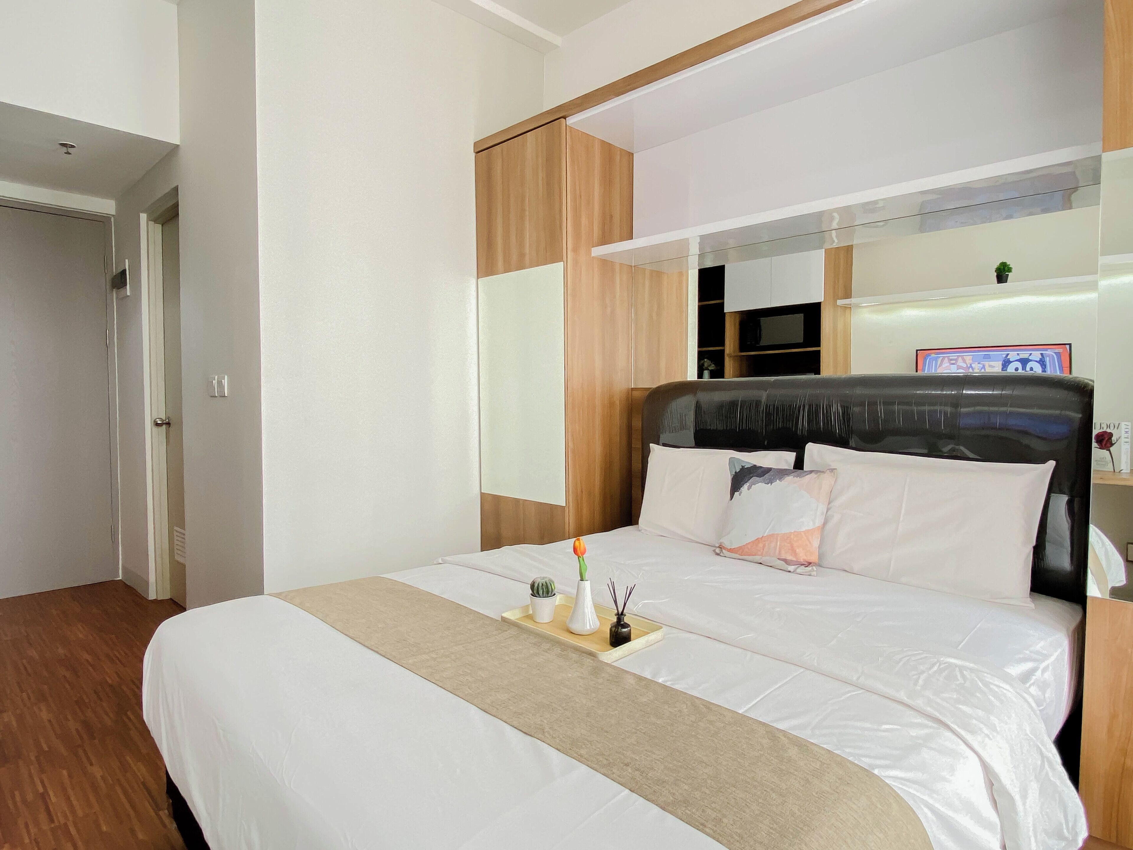A hotel room with a large bed, wooden headboard, a bedside table with a tray, and a mirror above the bed.