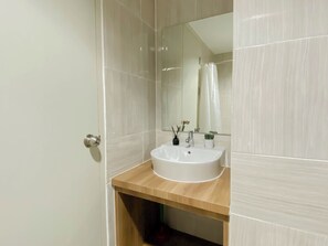 A bathroom with a white sink, a wooden countertop, a mirror, and a shower curtain. - Neat Restful Studio Room At Apartment Vasanta Innopark (Cikarang)