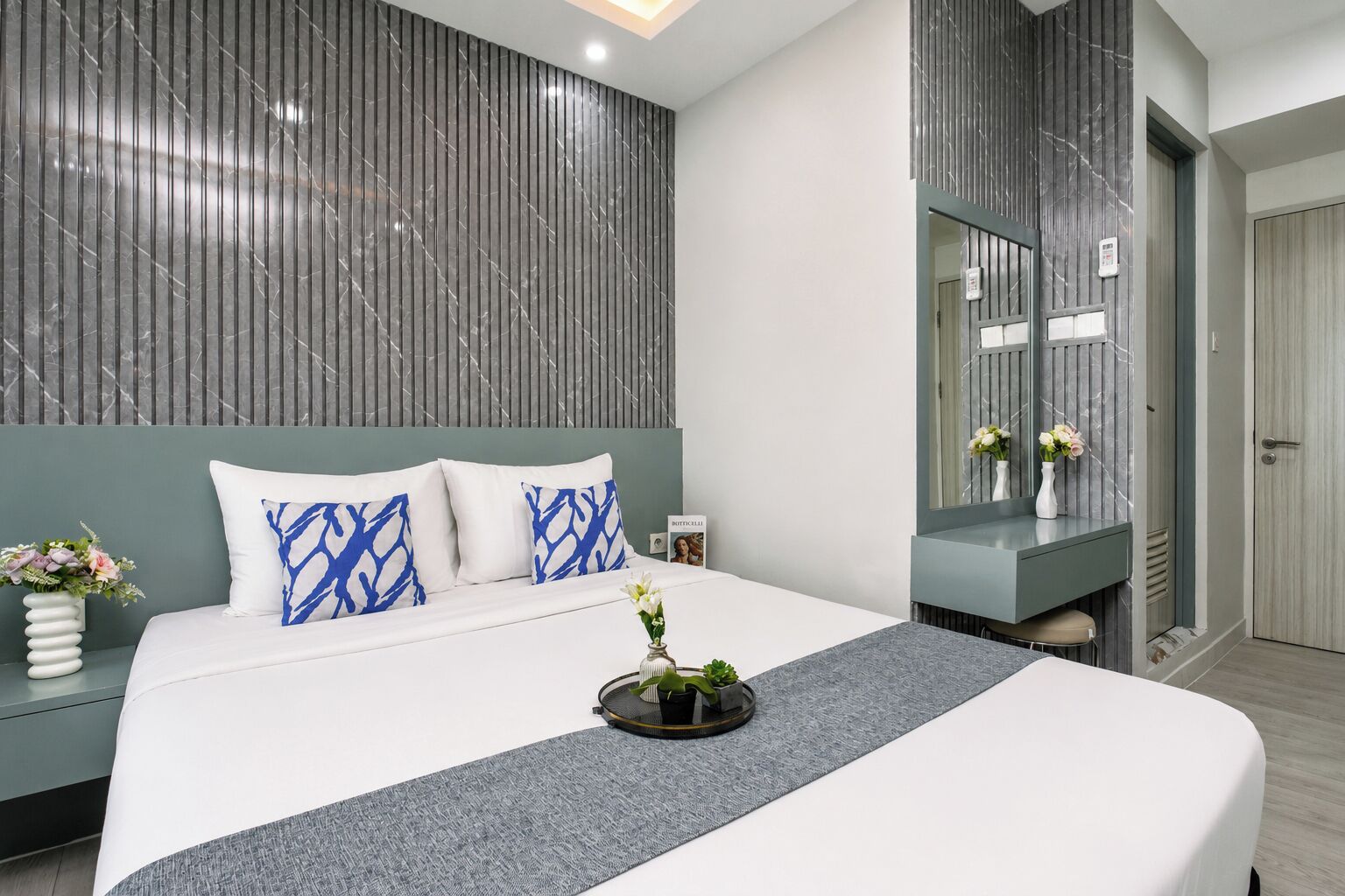 A modern bedroom with a large bed, a bedside table with a vase of flowers, and a wall-mounted mirror.