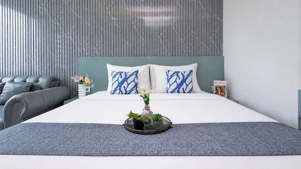 A modern bedroom with a large bed, grey upholstered sofa, and a decorative tray with flowers. - Calm Living In Gray Studio Room At Apartment Grand Kamala Lagoon (Bekasi)