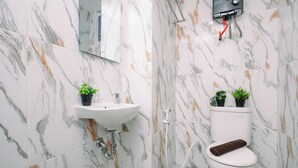 A bathroom with a white sink, two potted plants, a toilet, and a shower. - Calm Living In Gray Studio Room At Apartment Grand Kamala Lagoon (Bekasi)