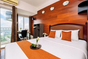 A hotel room with a large bed, a desk, a chair, a wardrobe, and a view of the city. - Homey Wooden Touch Studio Room At Apartment Grand Dhika City (Bekasi)