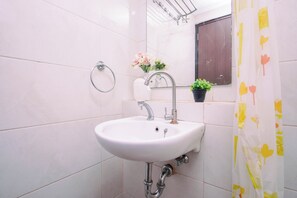 A bathroom with a white sink, a mirror, a towel rack, and a potted plant. - Homey Wooden Touch Studio Room At Apartment Grand Dhika City (Bekasi)