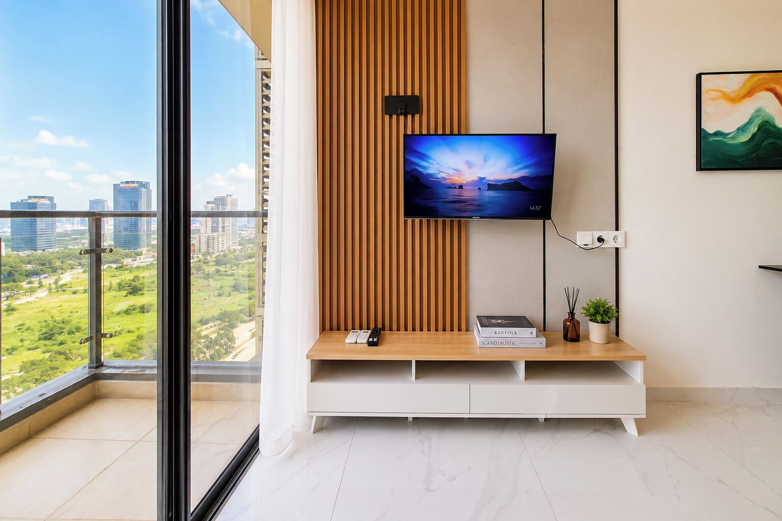 Una sala de estar moderna con un televisor grande montado en una pared de paneles de madera, un mueble blanco de entretenimiento debajo y una vista a la ciudad a través de un ventanal amplio.