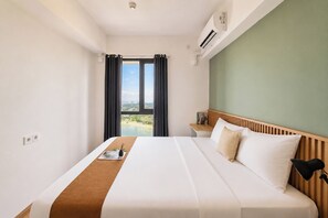 Ein Hotelzimmer mit einem Bett, einem Nachttisch, einer Lampe, einem Fenster mit Vorhängen und einer Klimaanlage.
