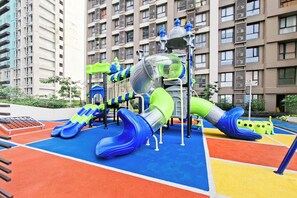 A playground with slides and climbing structures, surrounded by a multi-story building. - Chic Fully Furnished 2Br At Apartment Sky House Alam Sutera (Tangerang)