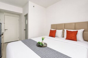Quarto de hotel com cama, mesa de cabeceira com planta e porta.