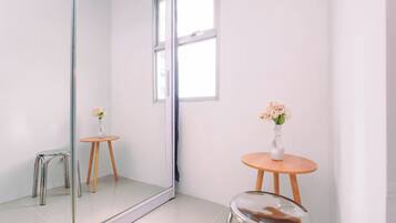 A minimalist room with a large mirror, a small stool, and a table with a vase of flowers.