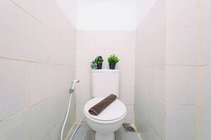 Een kleine betegelde badkamer met een toilet, een handdoek en twee planten in potten op de achterkant van het toilet.