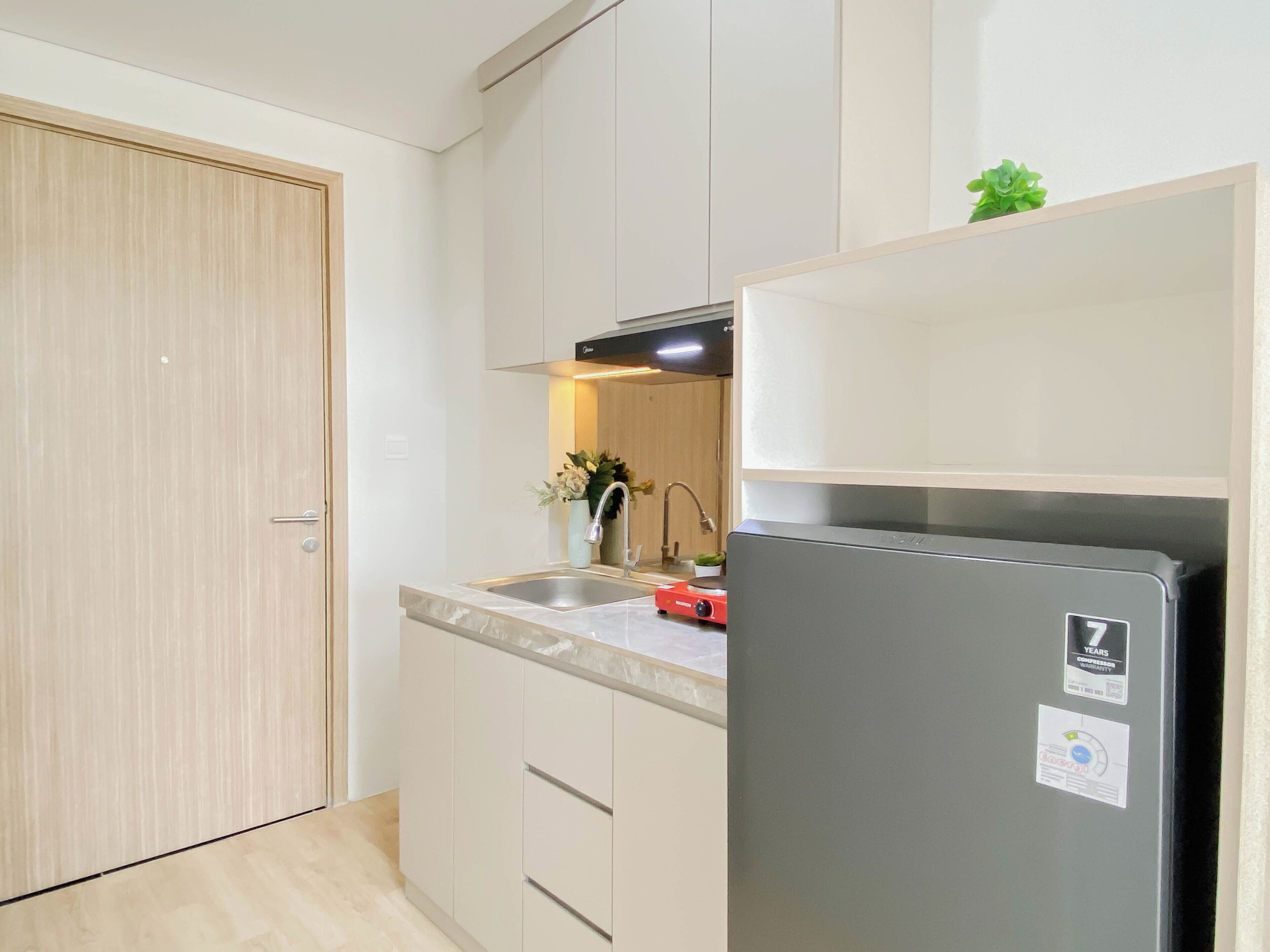 A compact kitchen with a built-in refrigerator, a sink, and a cabinet with a plant.