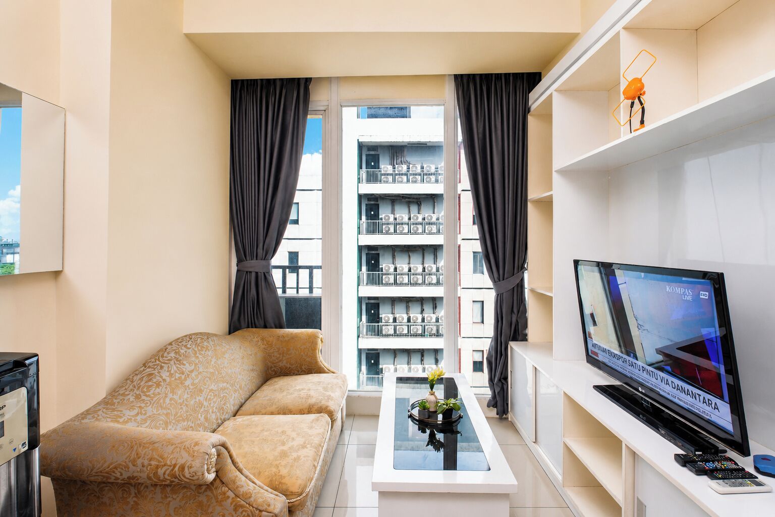 A modern living room with a sofa, a coffee table with a plant, a TV on a stand, and a balcony view.