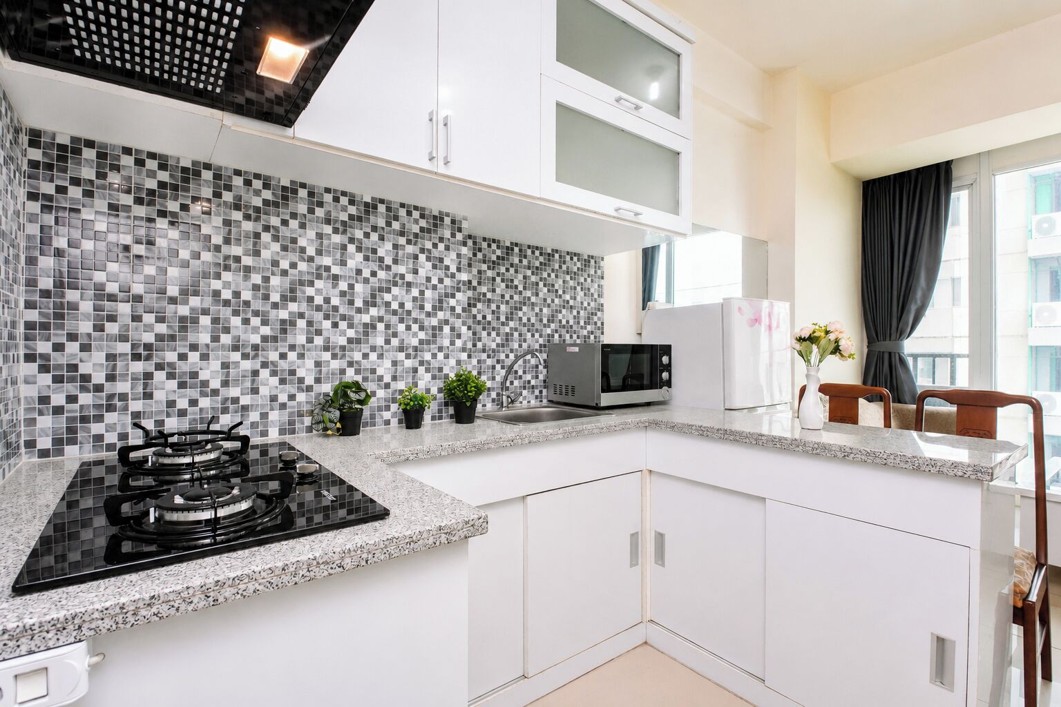 A modern kitchen with a black stove, a microwave, and a white refrigerator. There are potted plants on the counter and a window with curtains.