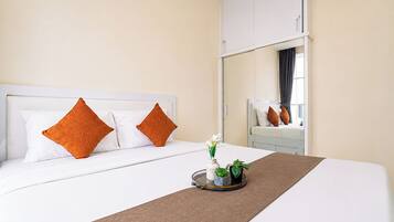 A hotel room with a bed, pillows, a bedside table with a vase and plants, and a mirror.